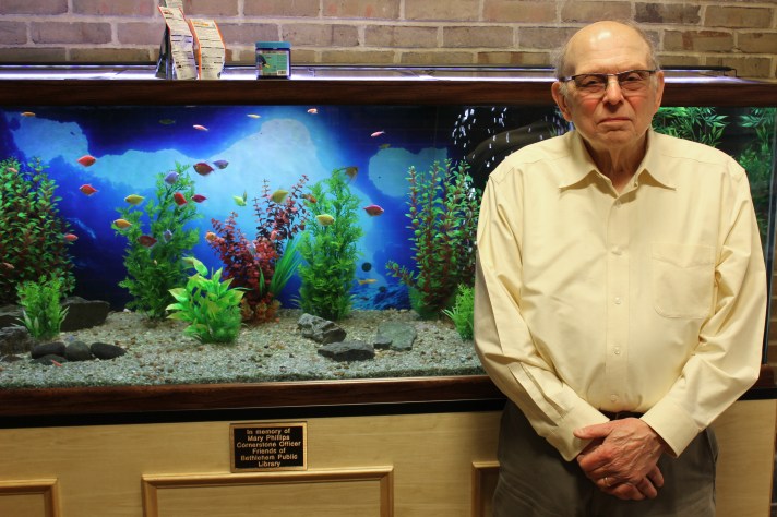 Bruce Phillips (in a yellow shirt) with the library's new fish tank and the plaque that honors his late wife, Mary.